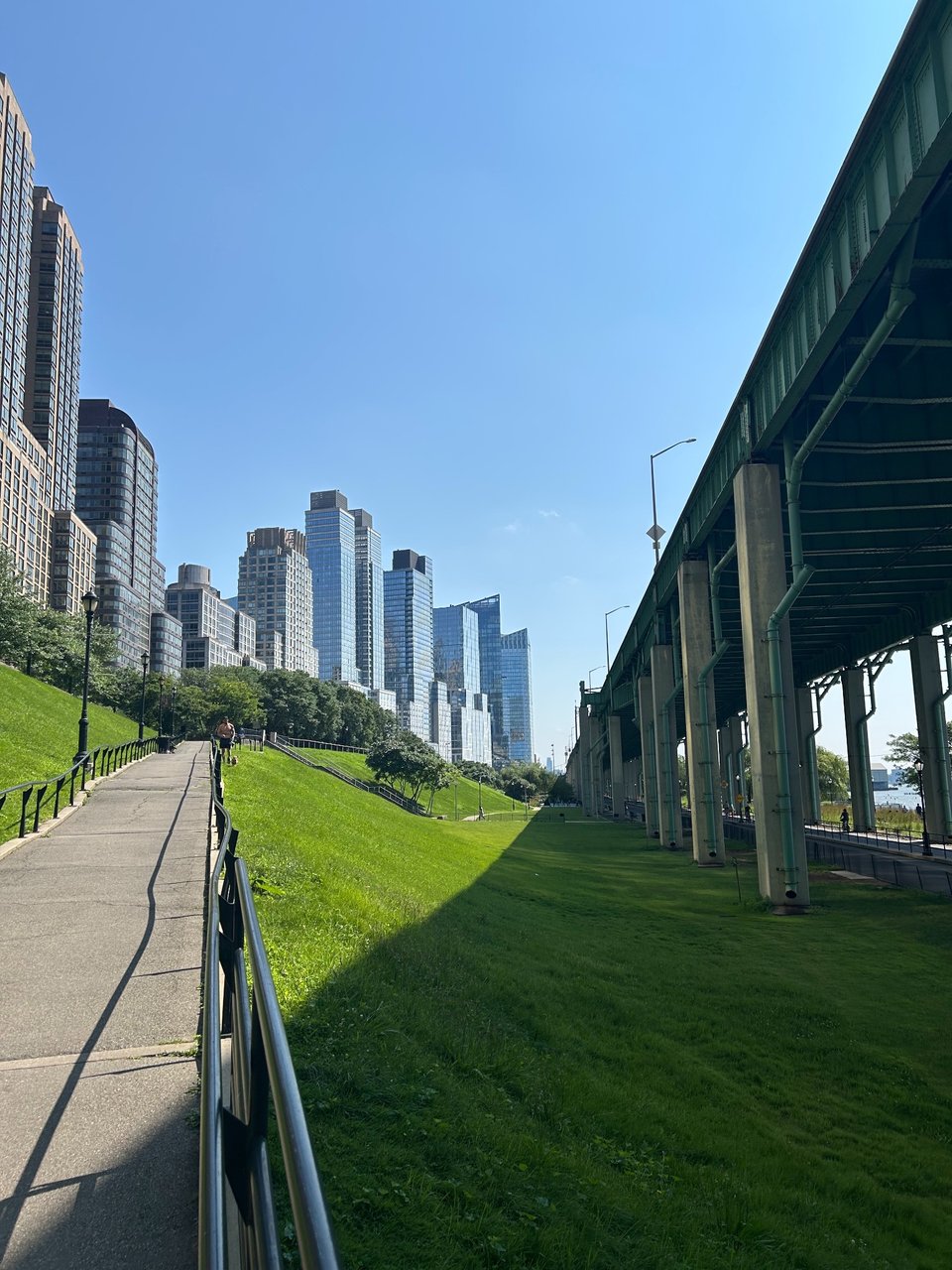 Sunny city path beside an elevated road and skyline